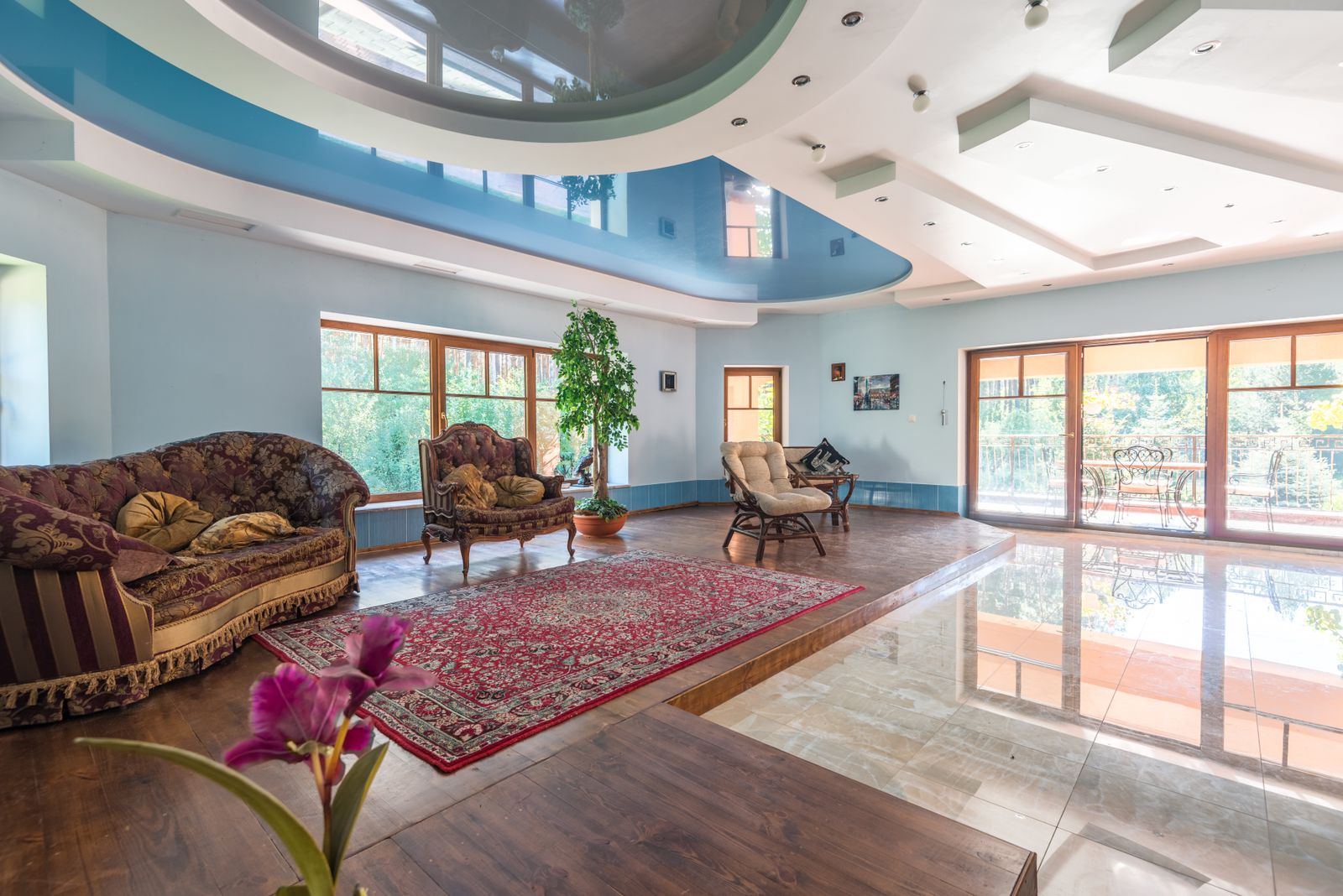 Spacious living room with a smooth, multi-level ceiling in white and blue tones, recessed lights, and large windows