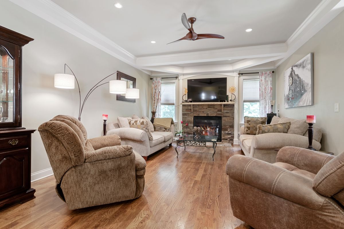Living room with a smooth white ceiling, crown molding, ceiling fan, and stone fireplace after refinishing